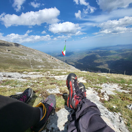 Bandiera italiana in lontananza e due escursionisti la guardano distesi atterra